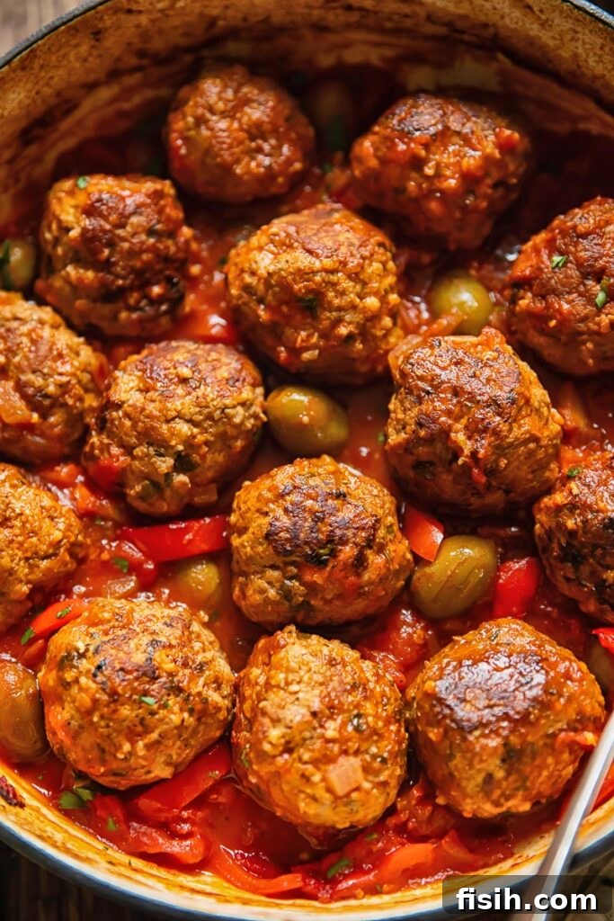Top down shot of pork and beef meatballs in a pot with tomato sauce topped with olives and red pepper slices, ready to be served
