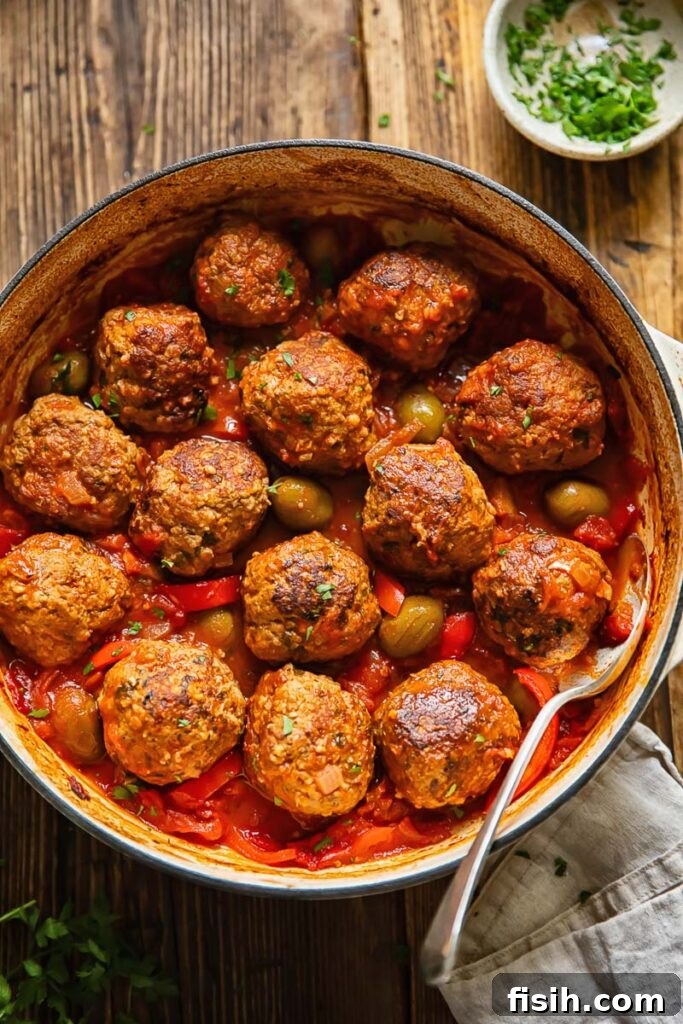 Spanish meatballs being scooped out of a pot with olive and tomato sauce, showcasing the rich texture and vibrant colors