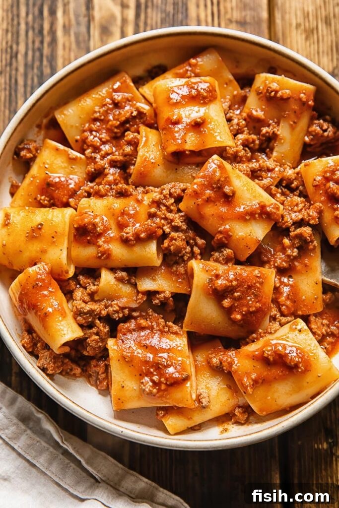 Top down shot of pasta with beef tomato sauce in a bowl with a fork topped with grated Parmesan
