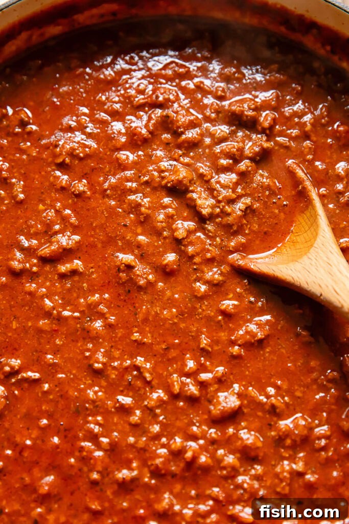 close up of a beef and tomato sauce in a pan with a wooden spoon in