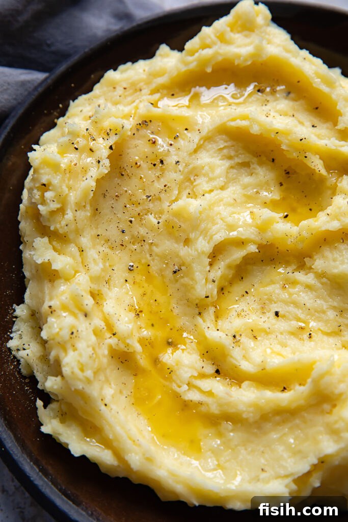 Top down shot of creamy Parmesan mashed potatoes swirled on a small plate, garnished with fresh grated Parmesan and cracked black pepper, ready to serve
