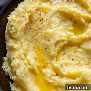 Top down shot of mashed potatoes swirled on a small plate topped with grated Parmesan and black pepper