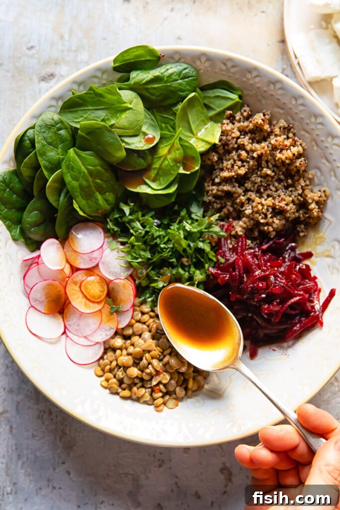 Beet and Lentil Quinoa Power Salad 5 Dressing being generously poured over a bowl of mixed quinoa, lentils, and vegetables.