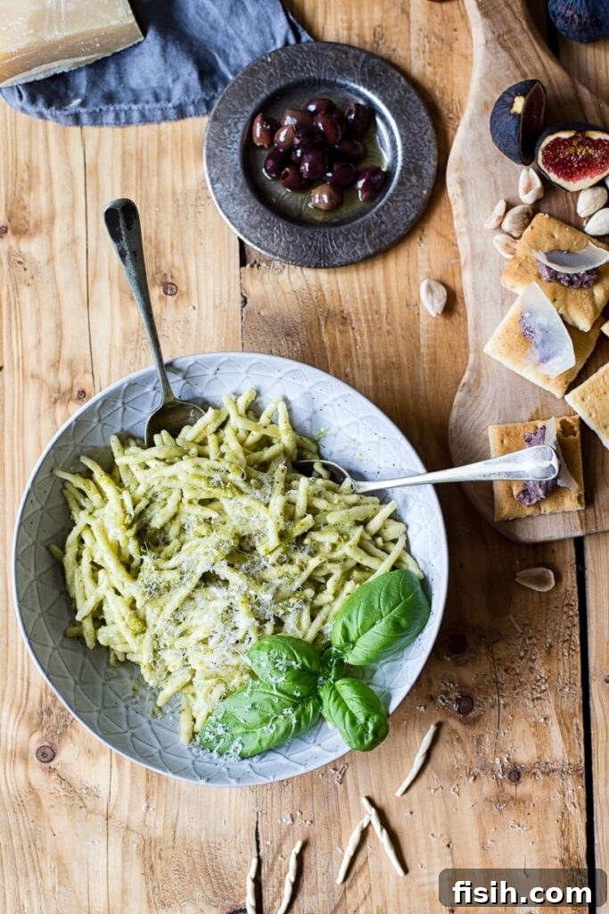 Bowl of pasta on wood table beside olives and cheese board