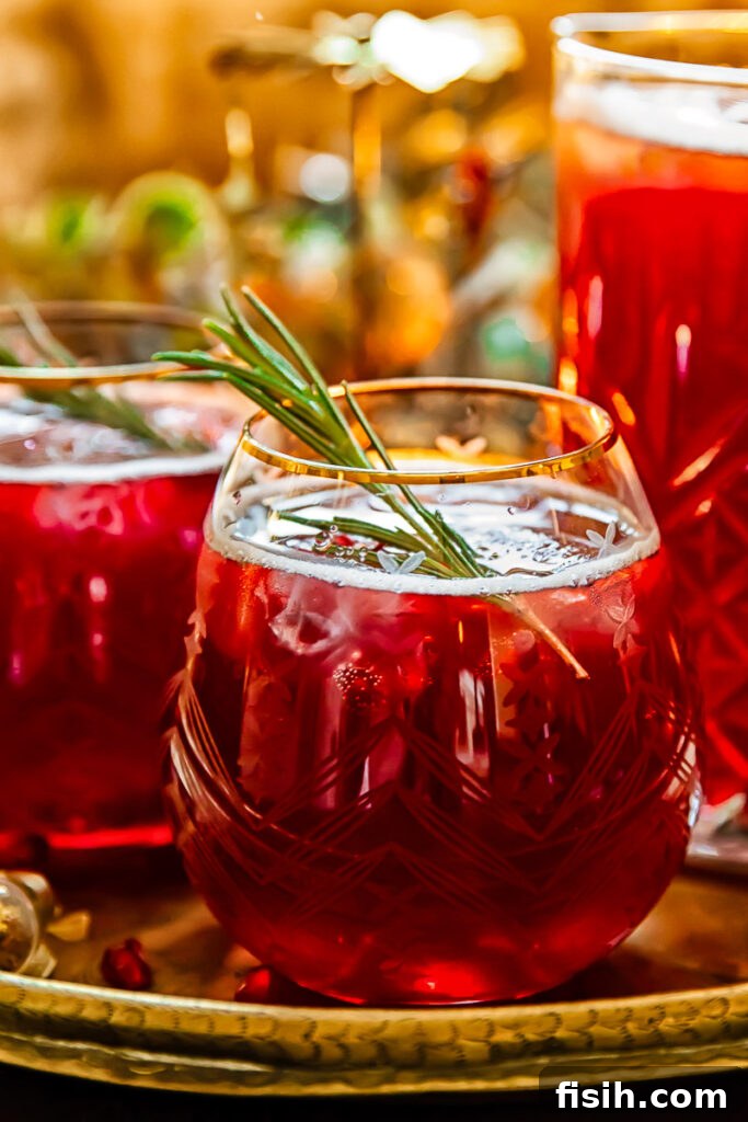 Side shot of pomegranate Christmas punch in a glass with rosemary garnish, ideal for festive gatherings.