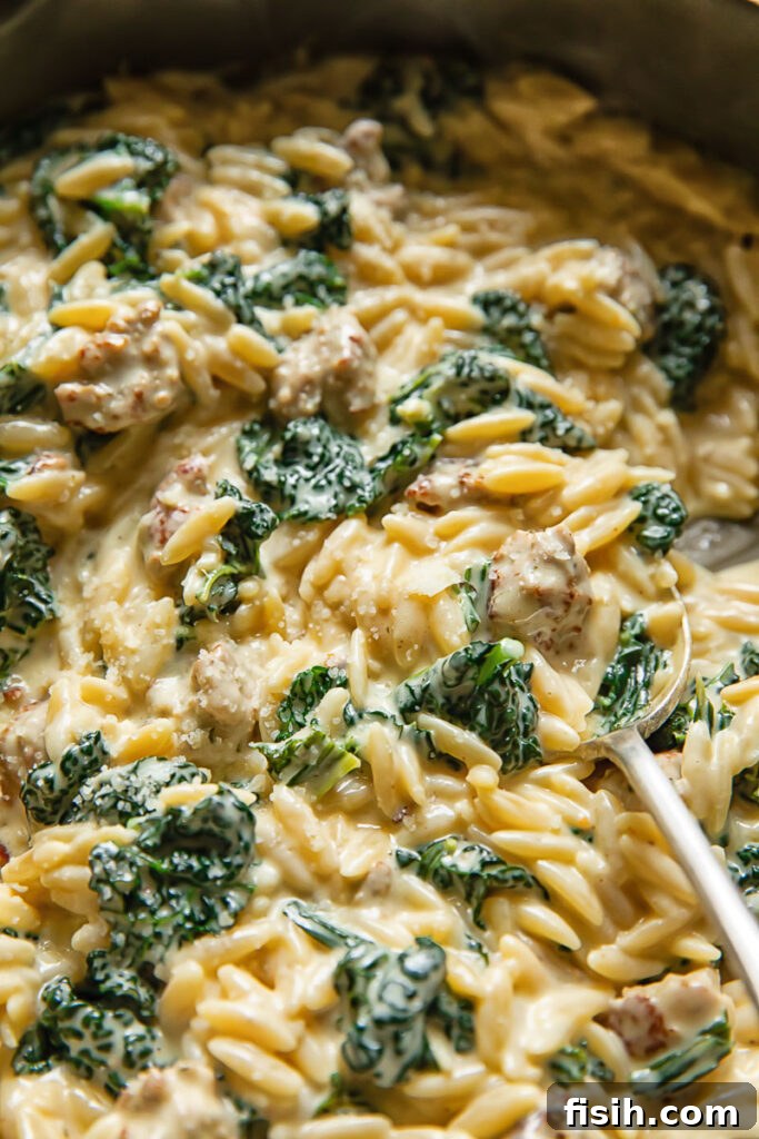 Close-up shot of creamy Italian sausage and kale orzo served in a bowl with a spoon, highlighting the rich texture and vibrant ingredients.