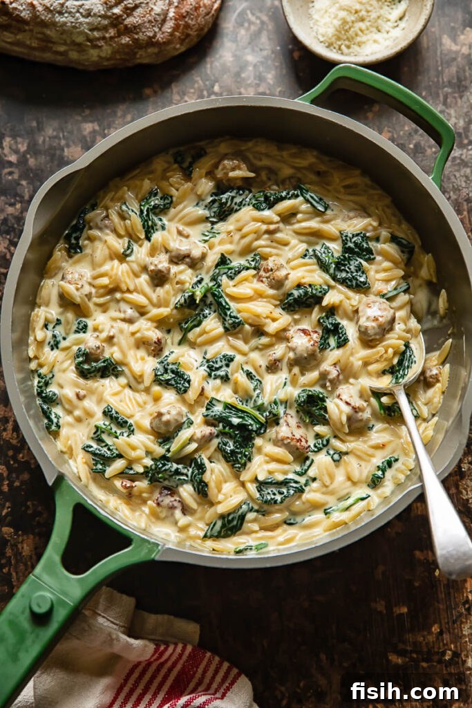 Top-down shot of Italian sausage and kale orzo simmering in a wide, shallow pan, showcasing its creamy texture and vibrant ingredients.