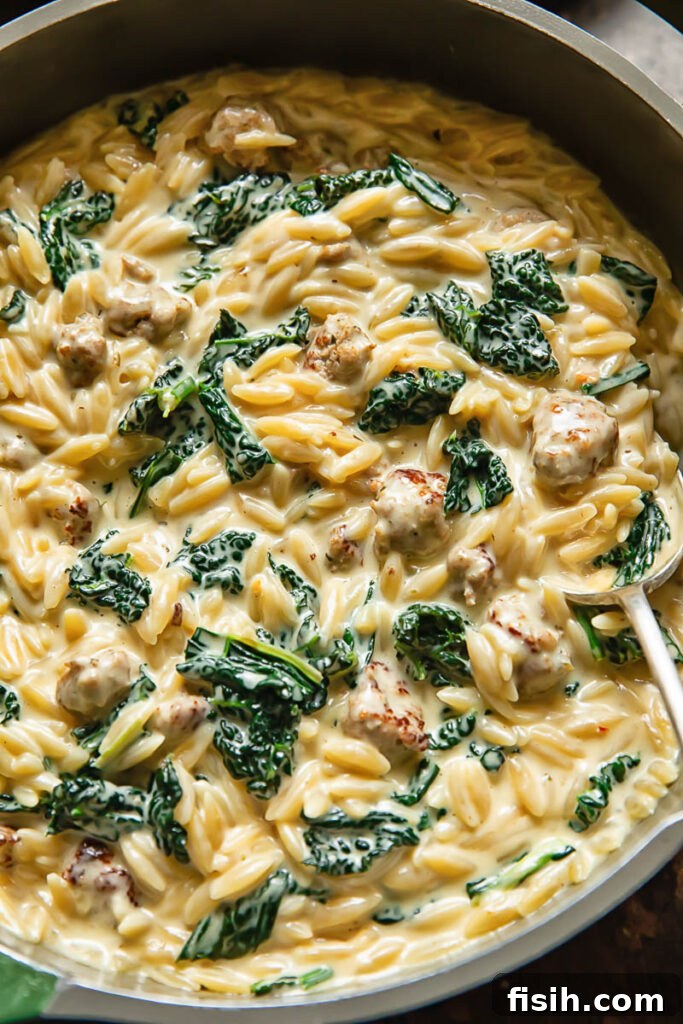 Shot of creamy Italian sausage orzo with vibrant kale and Parmesan cheese, presented in a rustic pan, ready to serve.