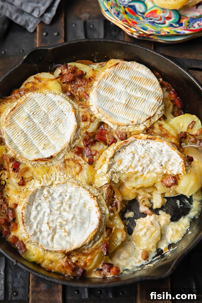 Top down shot of potato slices cooked in a pan with melted Camembert and bacon, showcasing the rich texture.