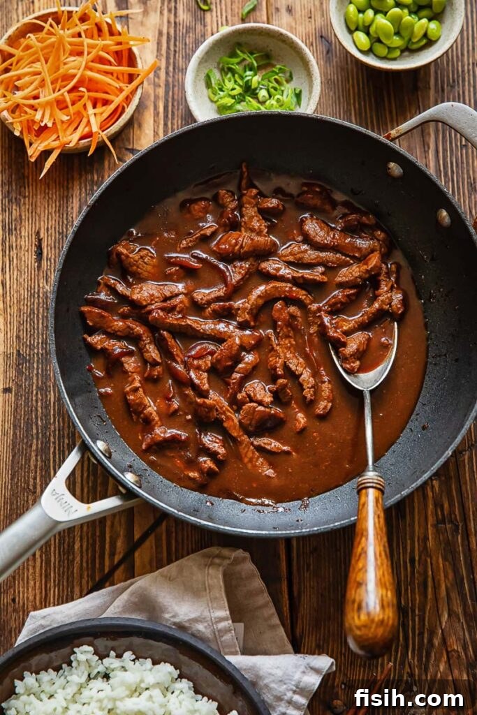 Top down shot of teriyaki beef stir fry in a pan next to bowls of sliced carrot and green onions