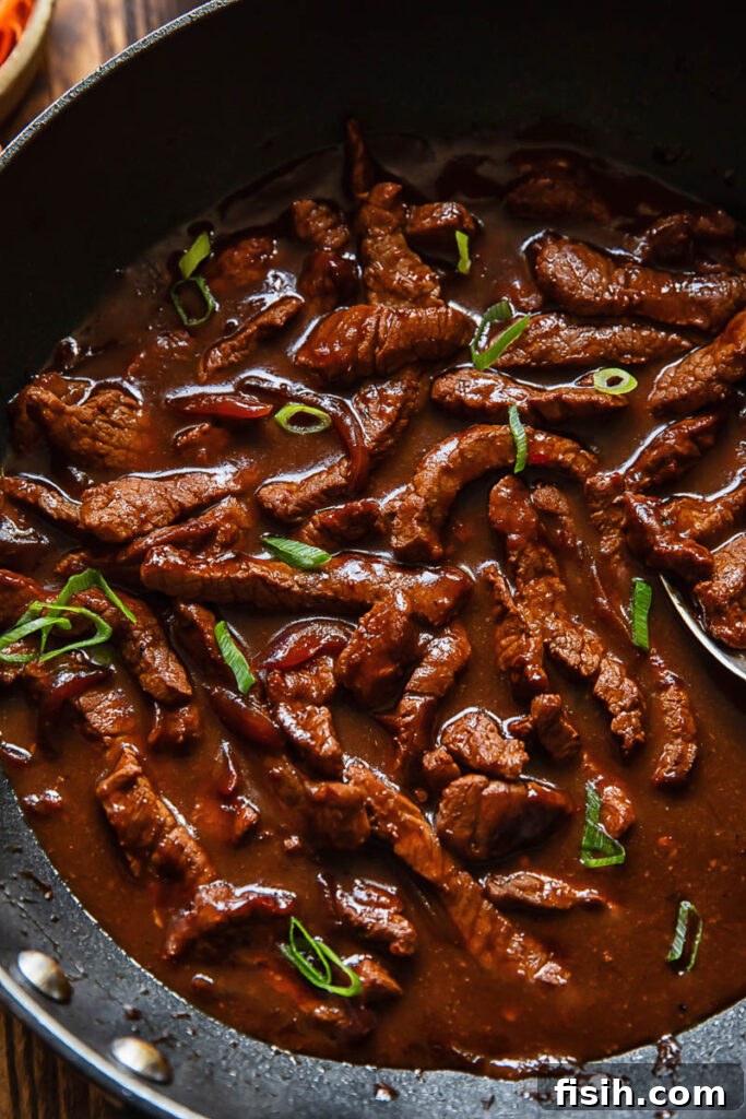 Close up shot of beef teriyaki in a deep wok topped with green onion