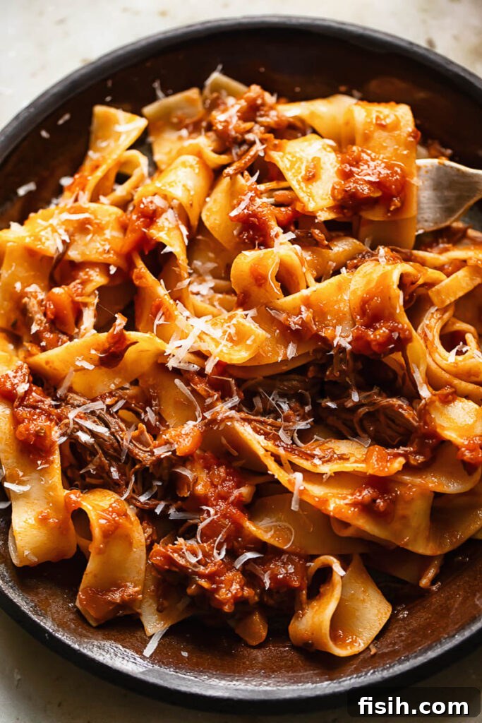 Close up shot of short rib ragu on a plate topped with grated Parmesan
