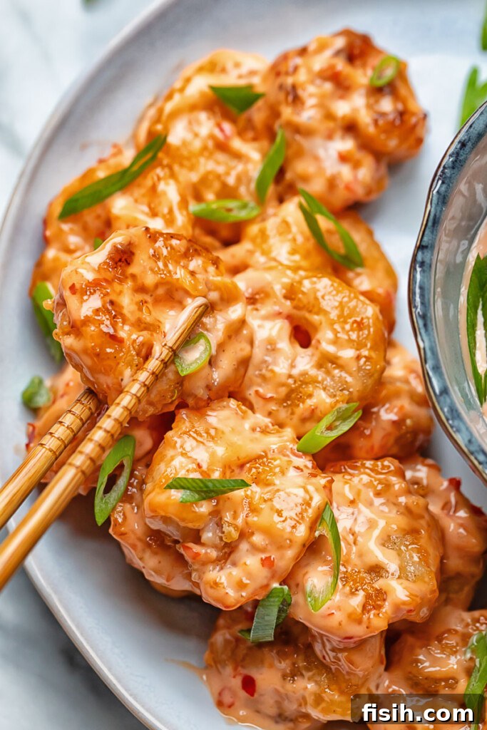 Close up shot of bang bang shrimp being picked up from a plate with chop sticks