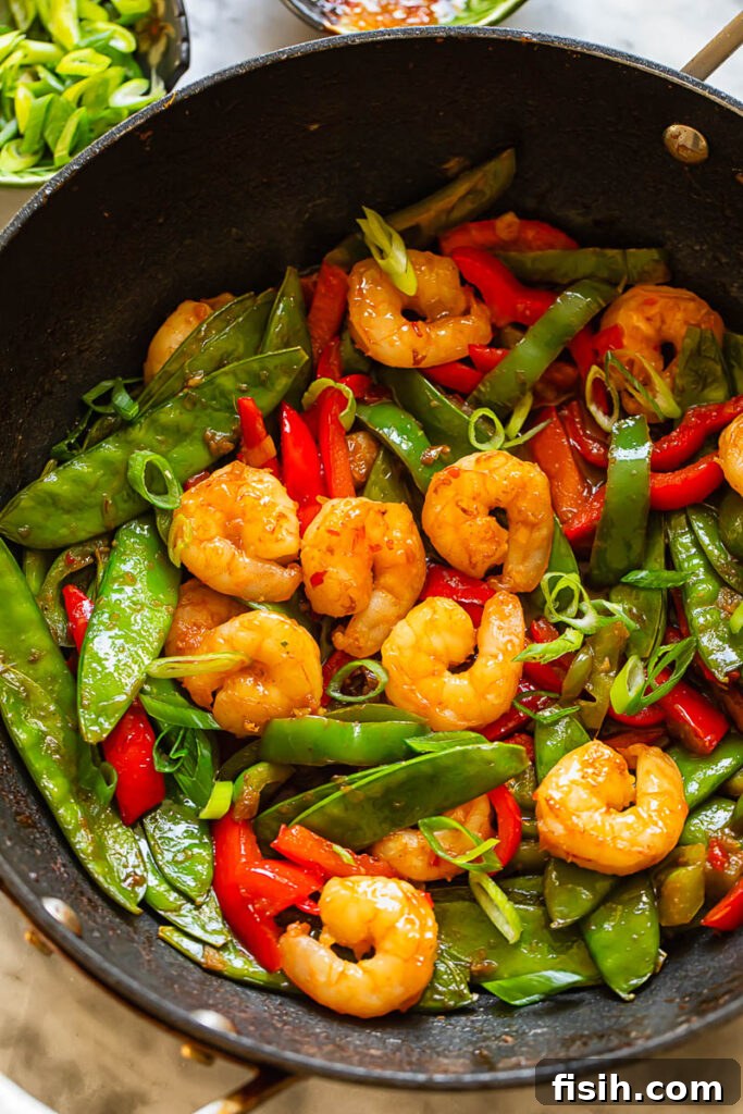 Top down shot of shrimp stir fry in a pan with veg topped with spring onions