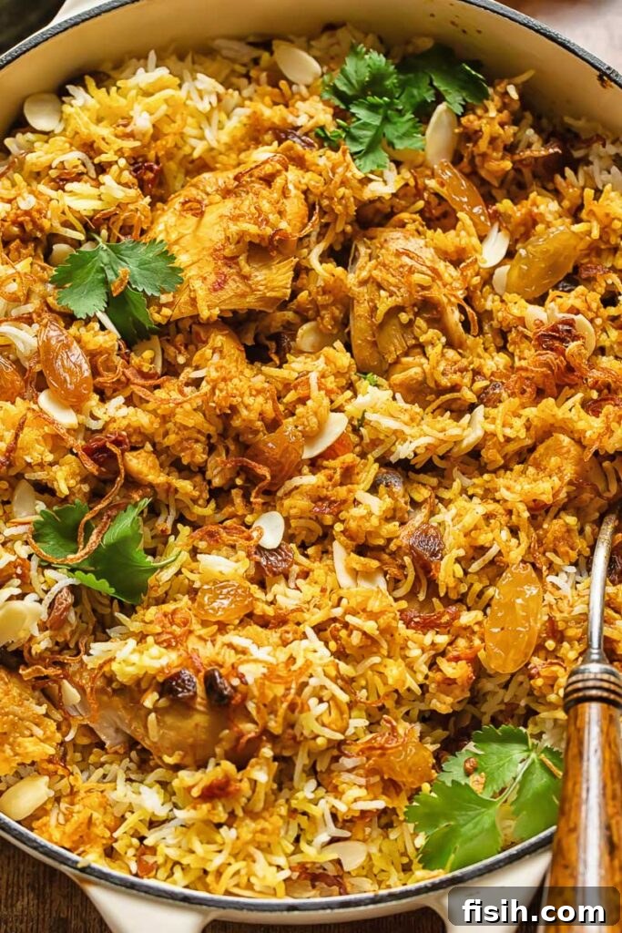 Effortless Chicken Biryani 2 Top down shot of chicken biriyani in a pan with roasted almonds and fresh parsley garnish, showcasing a vibrant and inviting meal.