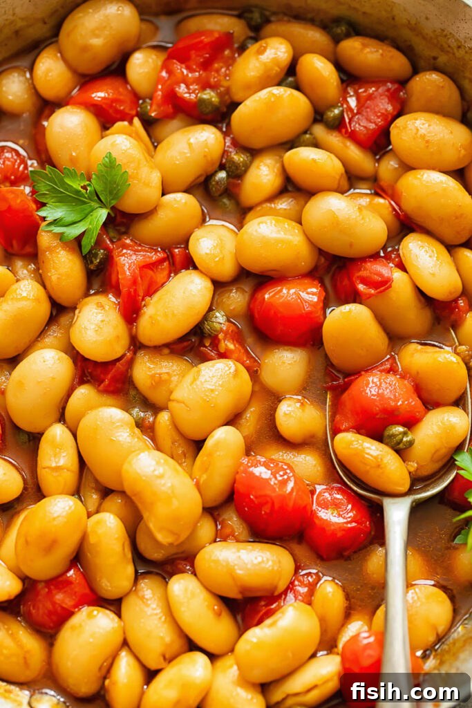 Creamy Butter Beans with Balsamic Burst Tomatoes 3 A close-up view of butter beans and cherry tomato sauce garnished with fresh basil, with a spoon resting in the pan, inviting you to taste.