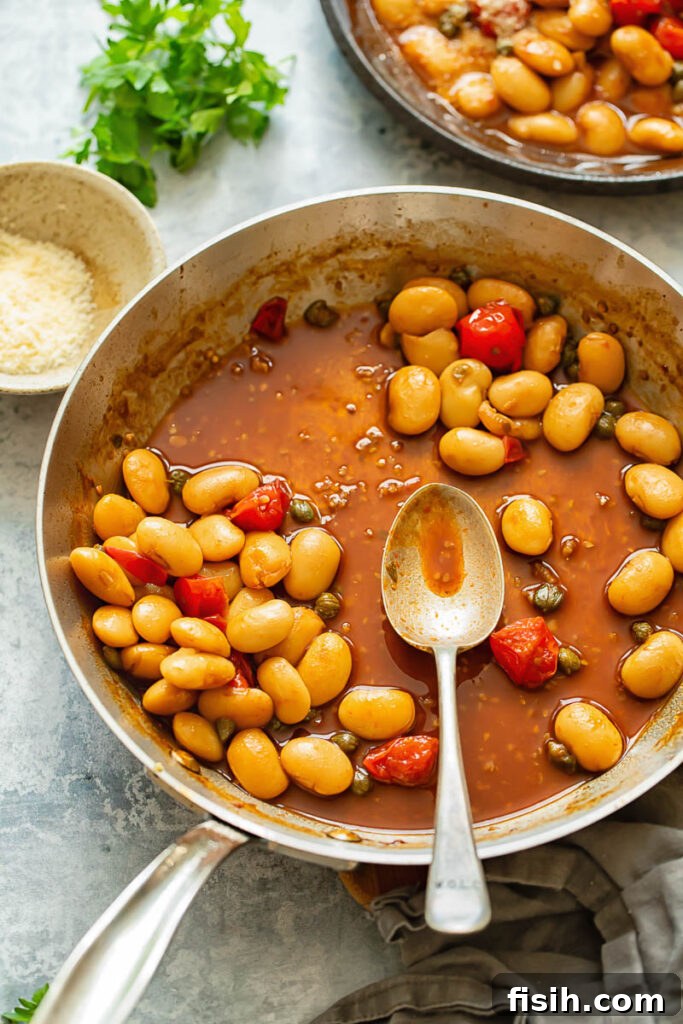 Creamy Butter Beans with Balsamic Burst Tomatoes 4 A tantalizing top-down shot of a spoon in a pan filled with rich butter beans and cherry tomato sauce, highlighting the rustic appeal of the dish.