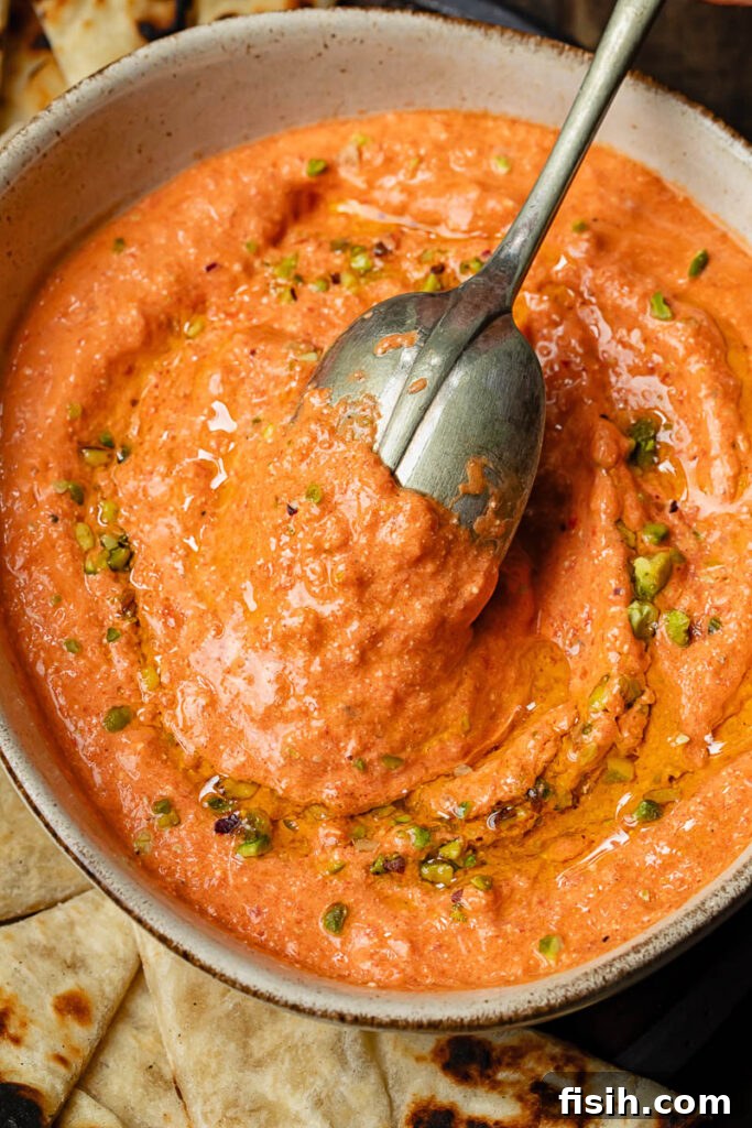 A vibrant top-down shot of creamy cottage cheese and red pepper dip served in a rustic bowl with a spoon, ready to be enjoyed.