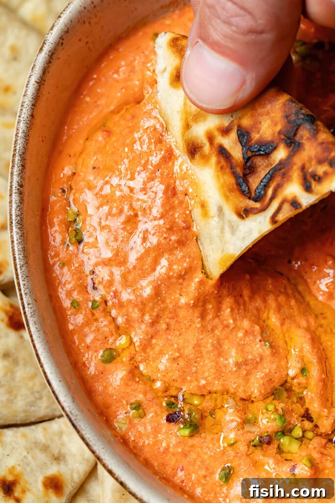 Close-up of freshly baked bread being dipped into a bowl of rich, smooth red pepper dip, highlighting its inviting texture.