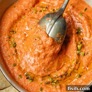 A top-down shot of creamy cottage cheese and red pepper dip in a bowl with a spoon, highlighting its inviting texture.