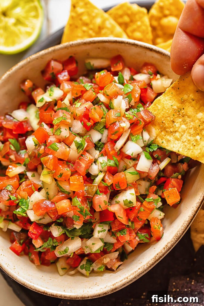 Close up shot of tortilla chip dipped in pico de gallo, showcasing its fresh ingredients and vibrant colors.