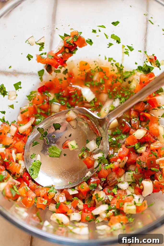 Top down shot of pico de gallo in a bowl with a serving spoon, highlighting the freshness and vibrant colors of the dish.
