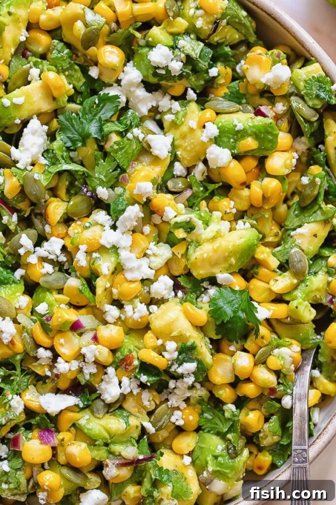 Close up of avocado corn salad topped with white cheese and cilantro, showcasing the vibrant colors and textures.