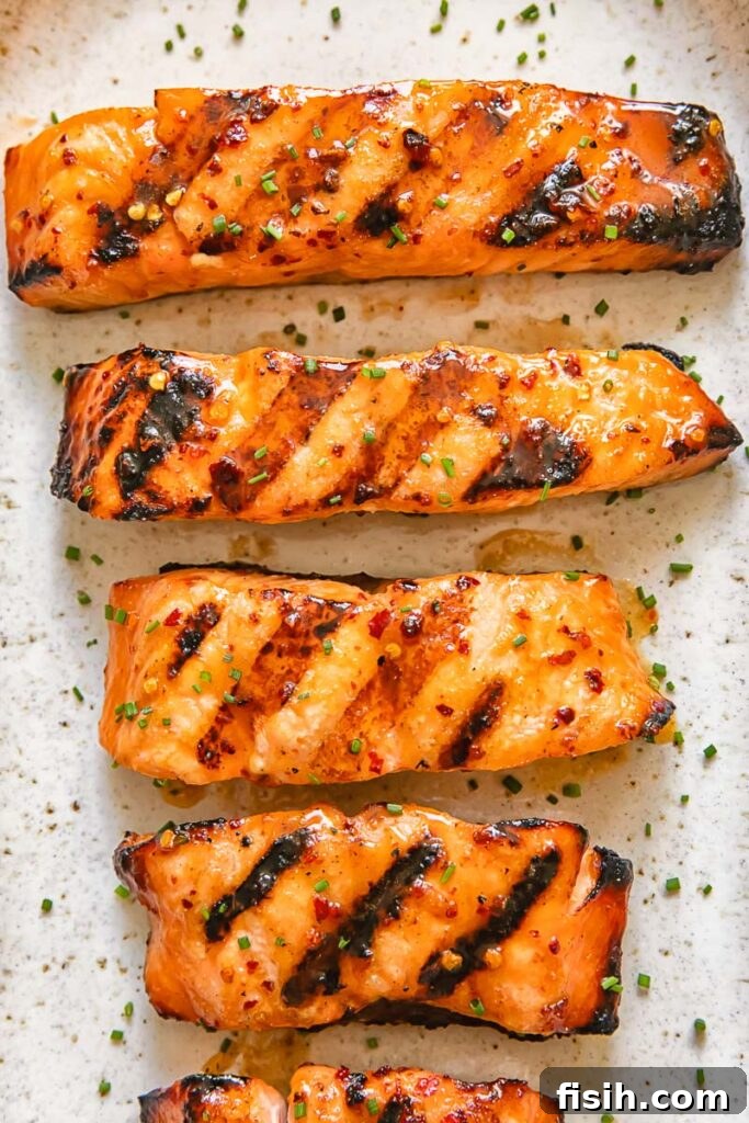 Top down shot of grilled maple glazed salmon on a serving platter with lemon slices and fresh herbs