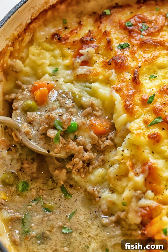 Close up of a serving of Shepherd's Pie being scooped from the dish, showing layers of meat, vegetables, and mashed potato.