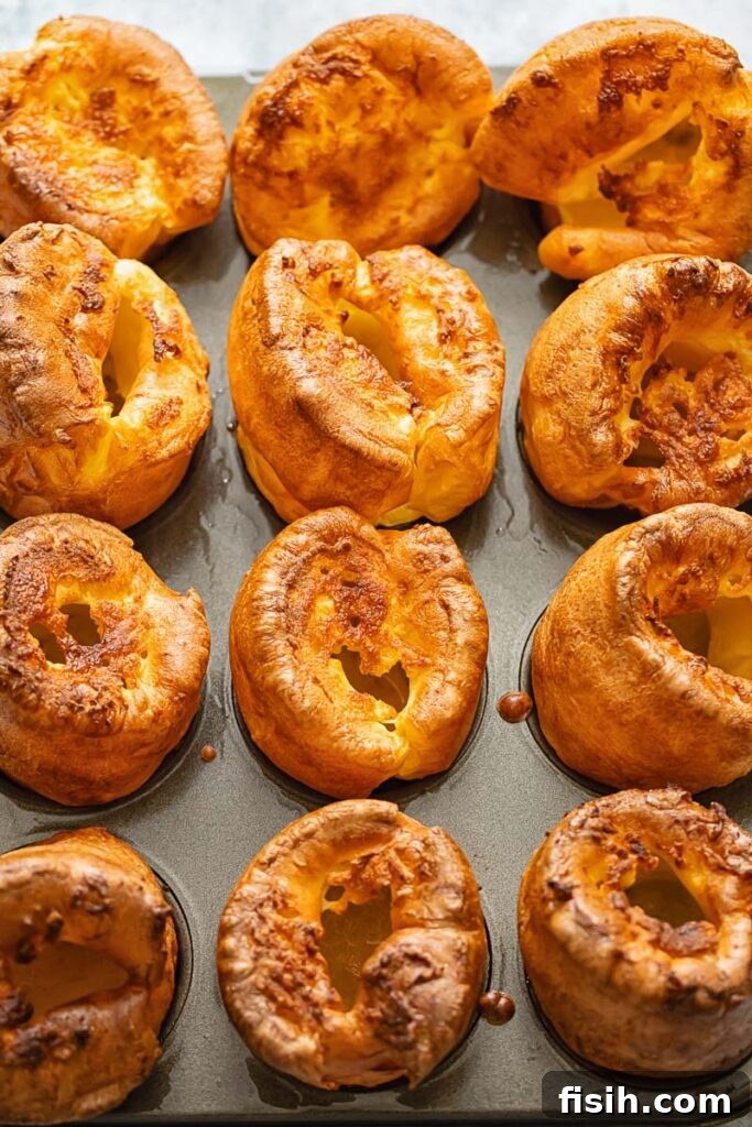 Rows of freshly baked, golden Yorkshire puddings cooling on a baking sheet, showcasing their impressive rise and texture.