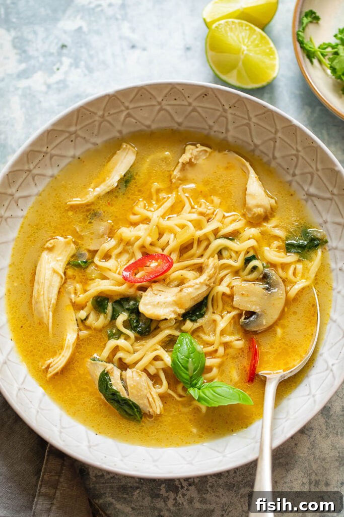A beautifully presented bowl of Thai chicken noodle soup with a spoon, highlighting its rich texture, vibrant colors, and succulent ingredients.