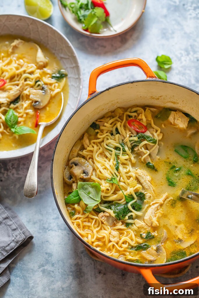A large pot of vibrant chicken noodle soup simmering on the stove, next to a beautifully arranged bowl, ready to be enjoyed.