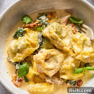 Bowl of tortellini with Tuscan sauce, garnished with fresh basil leaves.