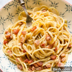 Bowl of spaghetti carbonara with a fork twirled, showing the creamy sauce and crispy pancetta.