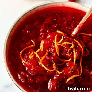 Homemade Cranberry Sauce with Port, richly colored and generously sprinkled with vibrant orange zest, served elegantly in a small glass bowl. A festive and flavorful holiday condiment.