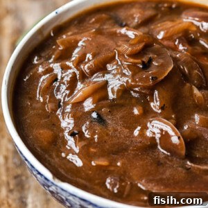 Side view of a serving bowl filled with glossy, rich Red Onion Gravy, perfectly thickened and ready to be poured generously over Thanksgiving dishes. A must-have for any holiday roast.