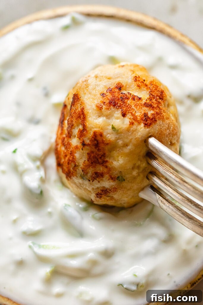 Close up of chicken meatball being dipped in tzatziki 