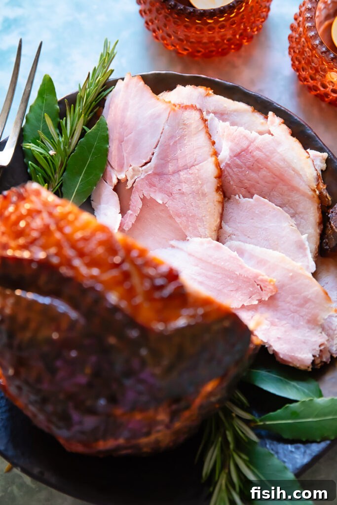 Sticky Sweet Bourbon Maple Ham 2 slices of glazed ham shown from the top down in a festive setting, with the glazed ham in the foreground