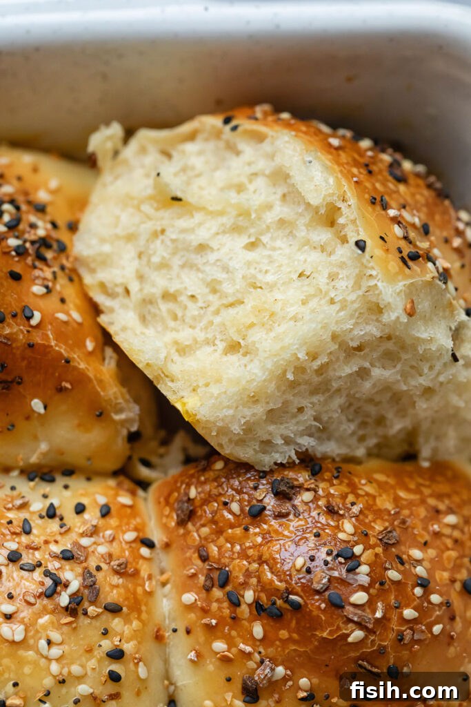 Close up of dinner roll being removed from baking dish, showcasing its golden crust and fluffy interior.