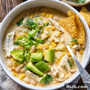 Top down view of a creamy white chicken chili with corn, green chilies, and avocado slices in a rustic bowl, ready to be enjoyed.