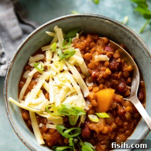 A hearty bowl of vegetarian chili, generously topped with grated cheese and a spoon ready to dive in, highlighting its rich, thick consistency.