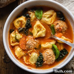 A comforting bowl of chicken meatball soup with tortellini, garnished with fresh herbs, showcasing its rich tomato base and hearty ingredients.