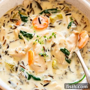 Creamy chicken wild rice soup served in a rustic bowl with a spoon, showing a rich, thick texture filled with tender chicken, vibrant carrots, and nutty wild rice.