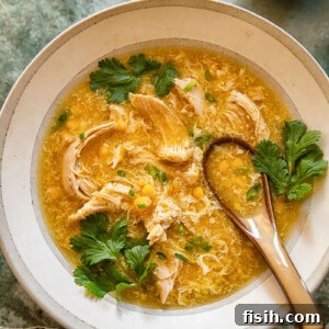 Top-down view of a vibrant chicken and sweetcorn soup in a bowl, showcasing its golden liquid and tender ingredients, garnished with fresh herbs.