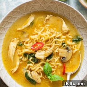 A rich and aromatic Thai chicken noodle soup, served in a beautiful bowl with a spoon, showing its creamy texture and fresh ingredients.