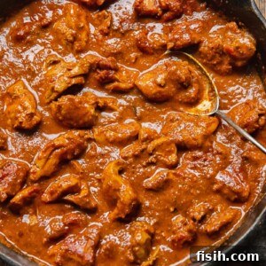 Close up of a pan of vibrant chicken rogan josh with a serving spoon.