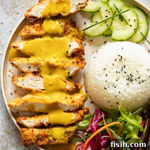 Crispy chicken katsu with a generous pouring of curry sauce, served alongside rice and sliced cucumber.