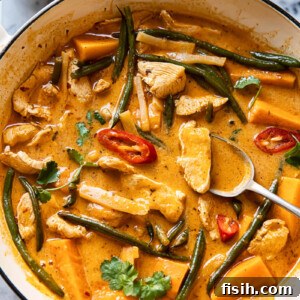 A white pan filled with vibrant Thai red curry, chicken, sweet potatoes, and green beans.