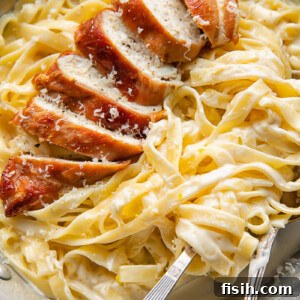 Creamy fettuccine topped with slices of prosciutto-wrapped chicken, garnished with fresh herbs, ready to be served.