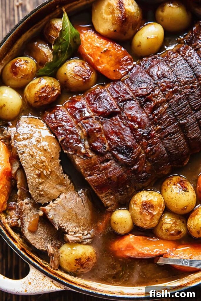 Close-up of a perfectly cooked beef pot roast and colorful root vegetables simmering gently in a large cast iron pot, showcasing the rich gravy.